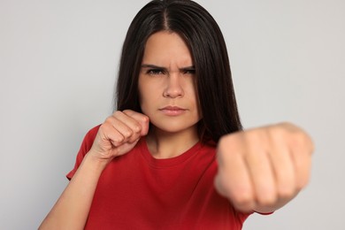 Young woman ready to fight on light grey background