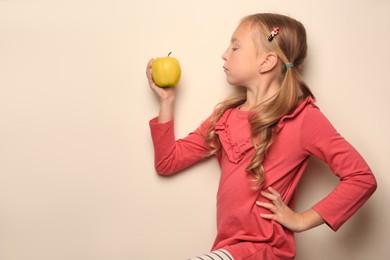 Photo of Cute little girl with apple on light background. Space for text