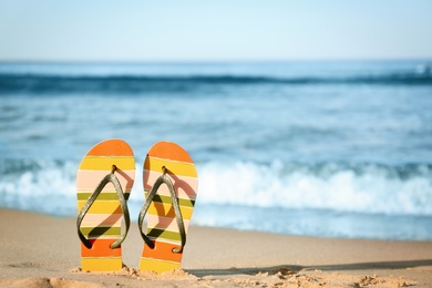 Stylish flip flops on sand near sea, space for text. Beach accessories