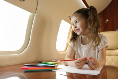Photo of Cute little girl drawing at table in airplane during flight