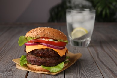 Photo of Tasty cheeseburger with patties and tomato on wooden table. Space for text