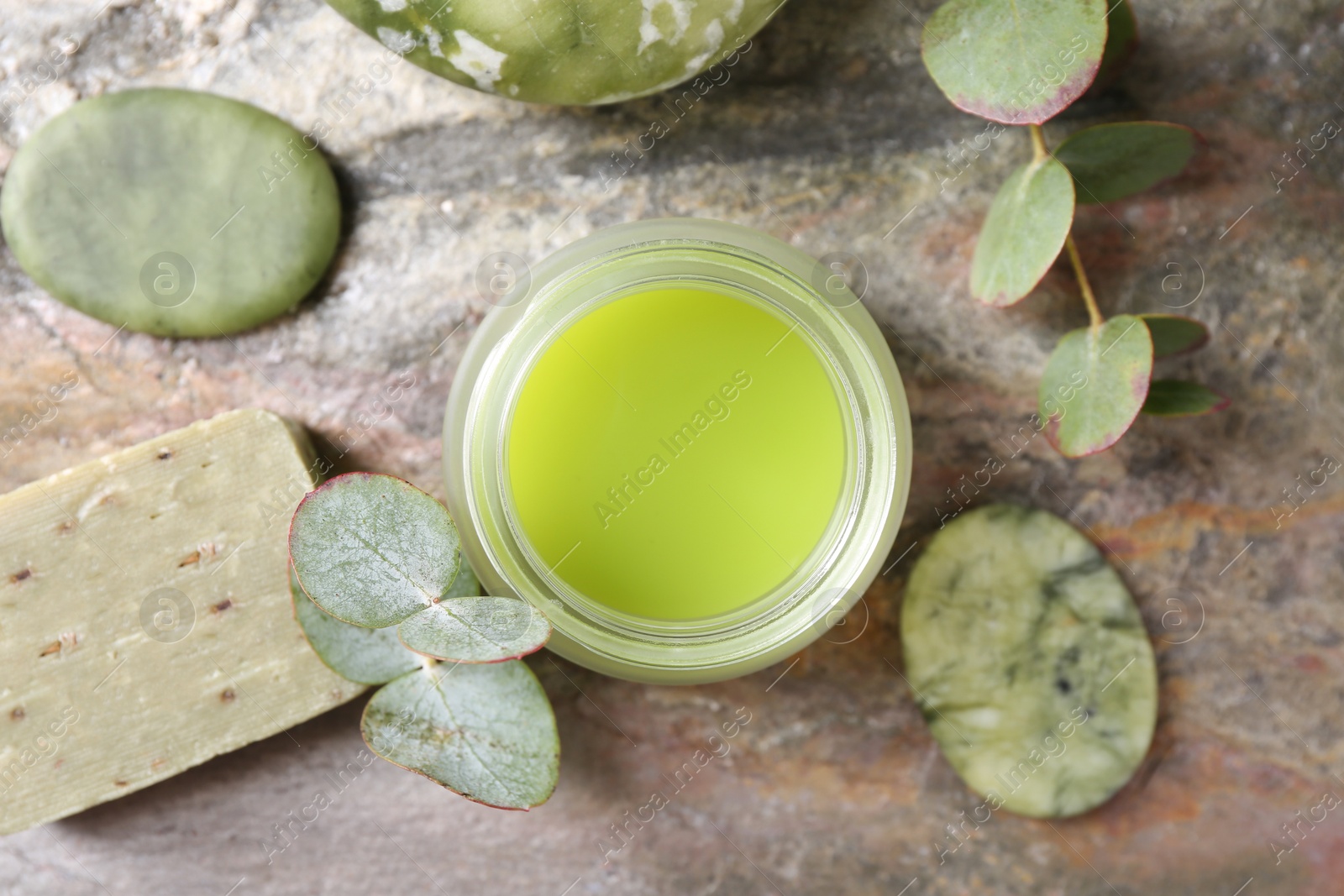 Photo of Jar of cream, spa stones, soap and eucalyptus branches on textured table, flat lay. Body care product