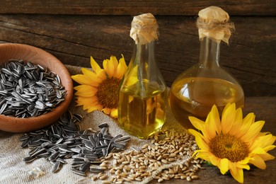 Bottles of sunflower oil, seeds and flowers on wooden table
