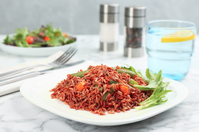 Photo of Tasty brown rice with vegetables on white marble table