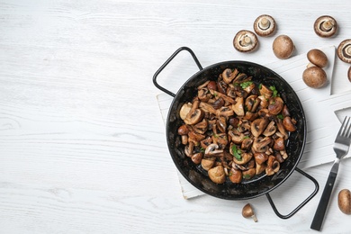 Photo of Frying pan with mushrooms on wooden background, top view. Space for text
