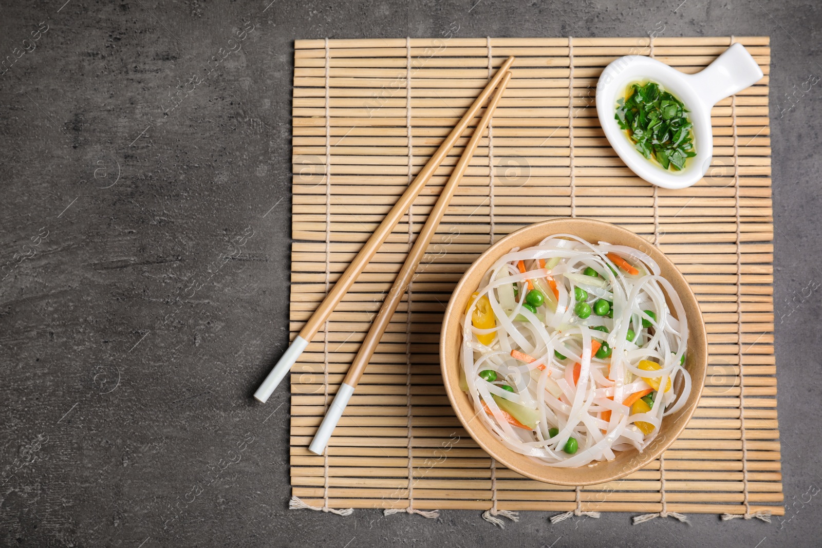 Photo of Flat lay composition with bowl of rice noodles and chopsticks on grey background. Space for text