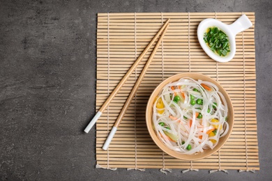 Flat lay composition with bowl of rice noodles and chopsticks on grey background. Space for text