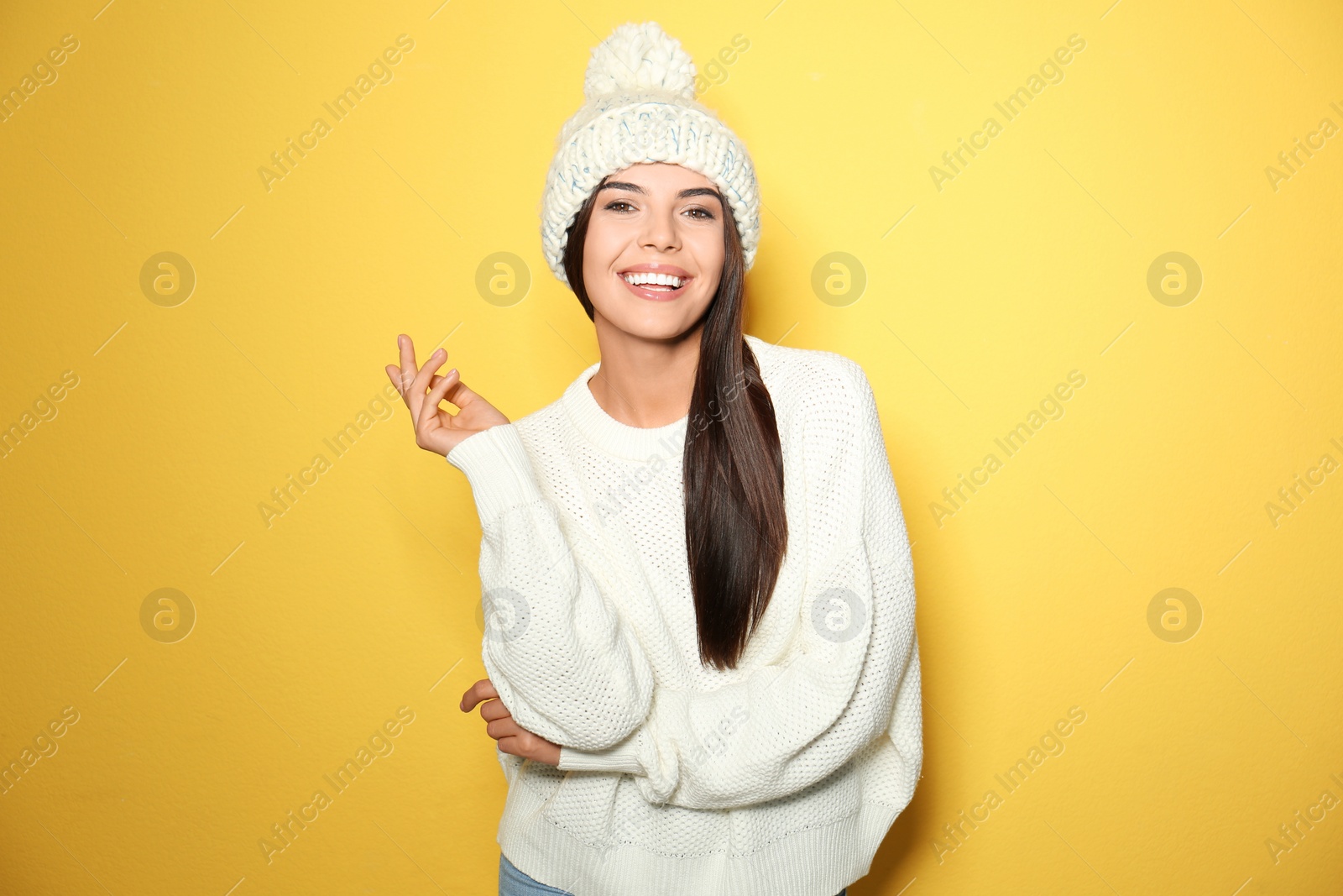 Image of Happy young woman wearing warm sweater and knitted hat on yellow background