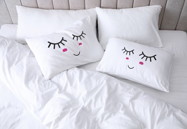 Soft pillows with cute faces on comfortable bed, above view