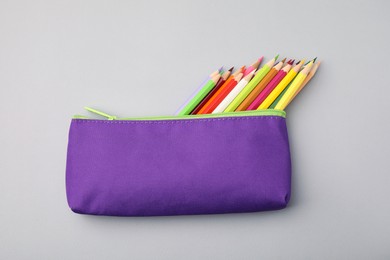 Many colorful pencils in pencil case on light grey background, top view