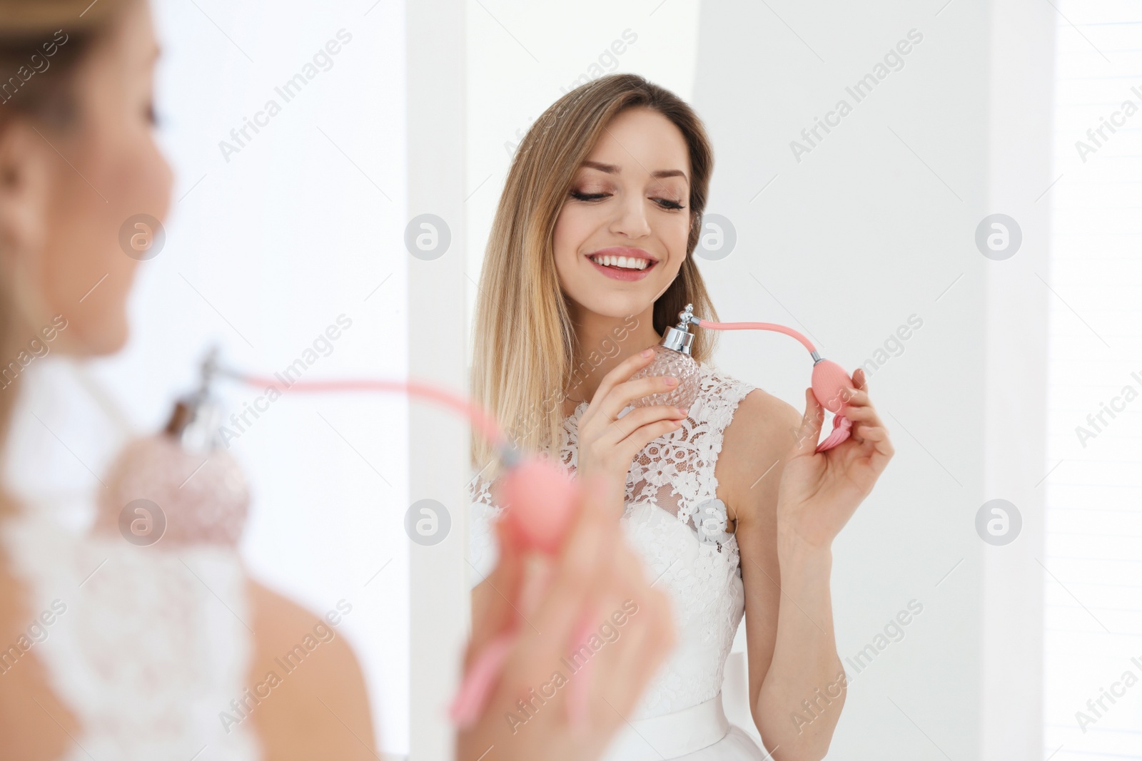 Photo of Beautiful young bride with bottle of perfume near mirror indoors