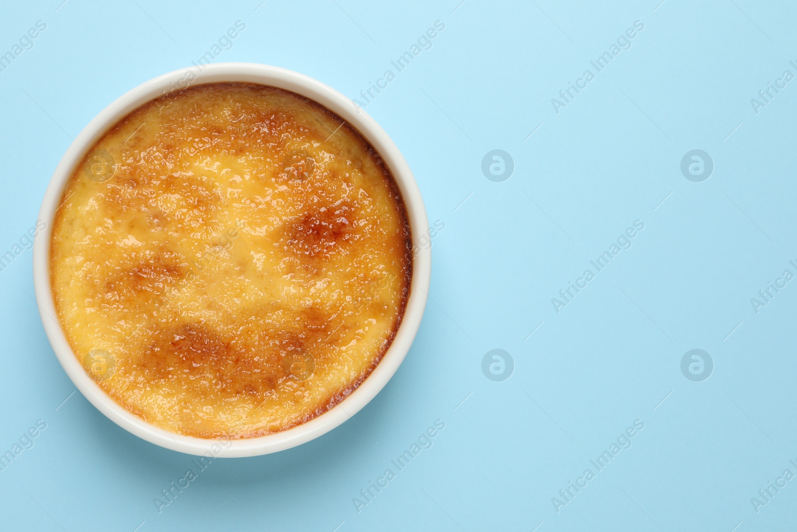 Photo of Delicious creme brulee on light blue background, top view. Space for text