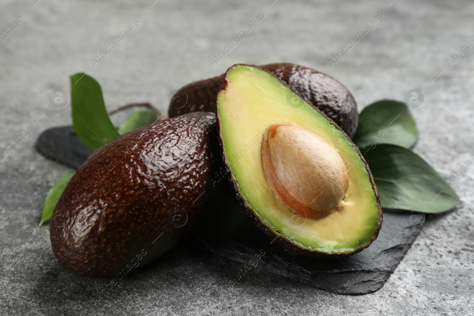 Photo of Whole and cut avocados with green leaves on grey table, closeup