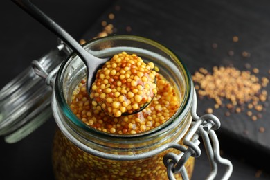 Photo of Taking whole grain mustard with spoon from jar on table, closeup