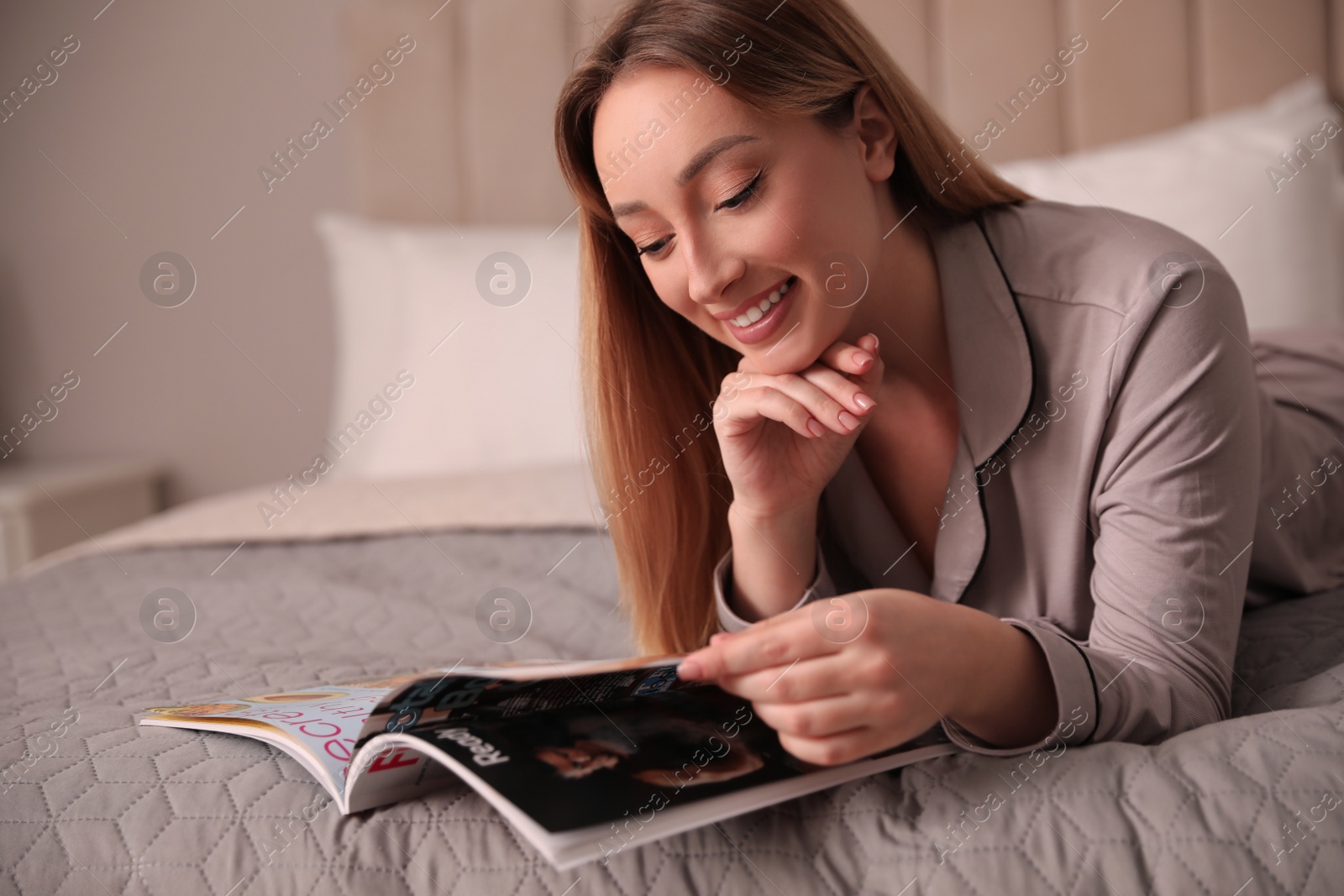 Photo of Happy woman reading magazine on bed indoors