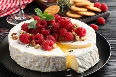 Photo of Brie cheese served with raspberries and walnuts on black wooden table, closeup