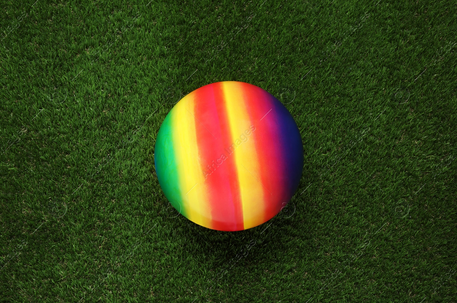 Photo of New bright kids' ball on artificial green grass, top view