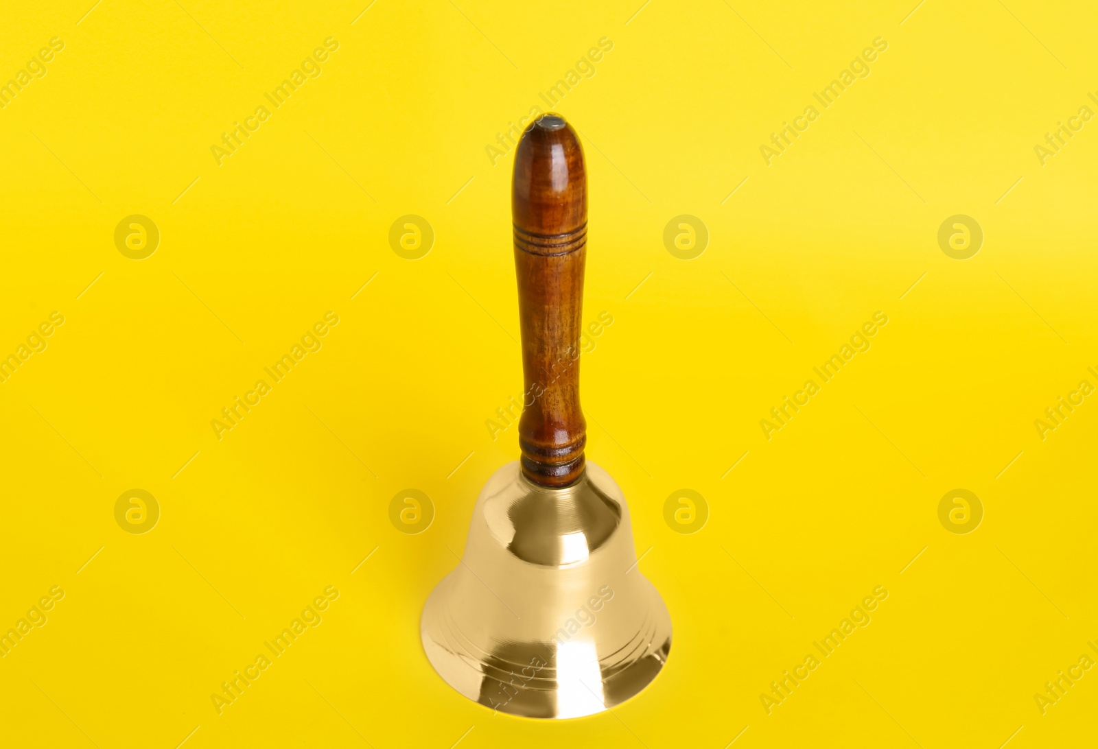 Photo of Golden school bell with wooden handle on yellow background