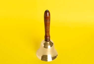 Photo of Golden school bell with wooden handle on yellow background