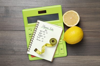 Photo of Notebook with products of low glycemic index, calculator, measuring tape and lemons on wooden table, flat lay