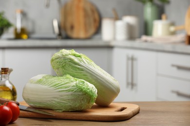 Photo of Fresh Chinese cabbages, knife, tomatoes and oil on wooden table in kitchen, space for text