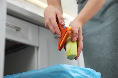 Photo of Woman peeling fresh zucchini above garbage bin indoors, closeup