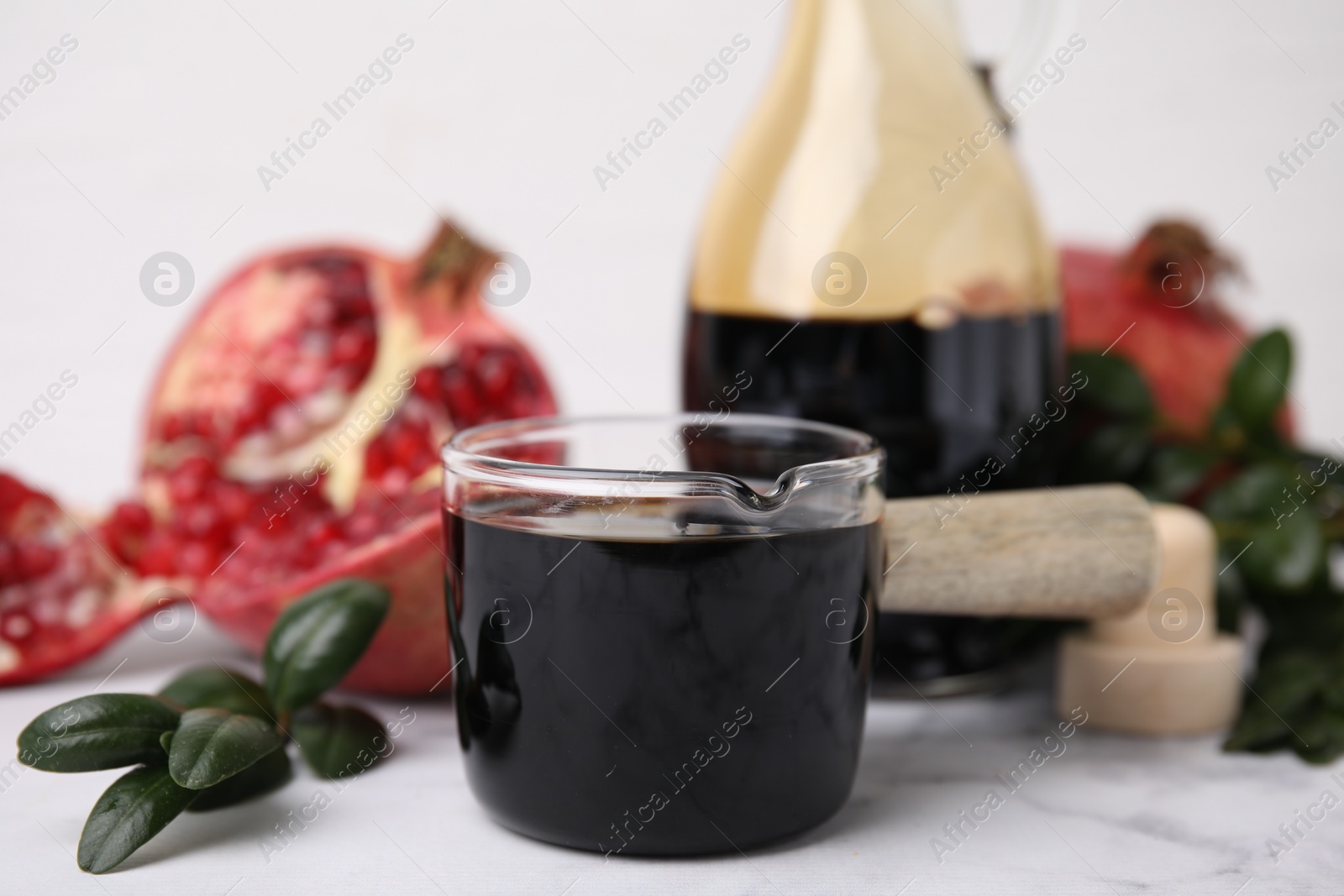 Photo of Tasty pomegranate sauce and branch on white marble table, closeup