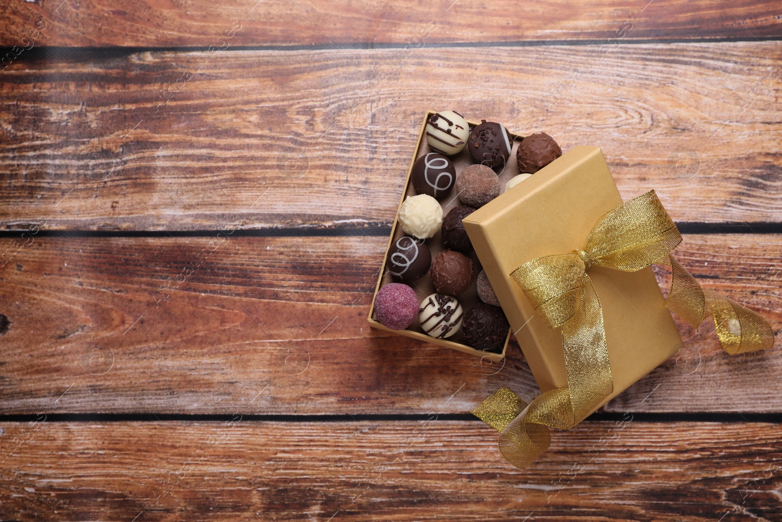 Open box with delicious chocolate candies on wooden table, top view. Space for text Photo of Open box with delicious chocolate candies on wooden table, top view. Space for text
