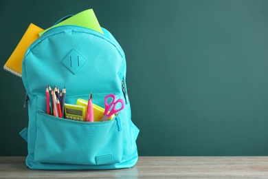 Photo of Bright backpack with different school stationery on wooden table near green chalkboard. Space for text