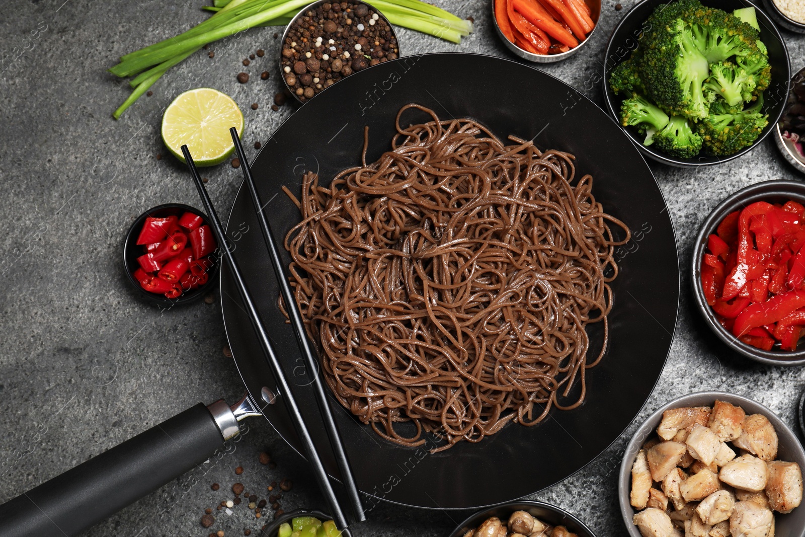 Photo of Wok with noodles, chicken and other products on grey table, flat lay