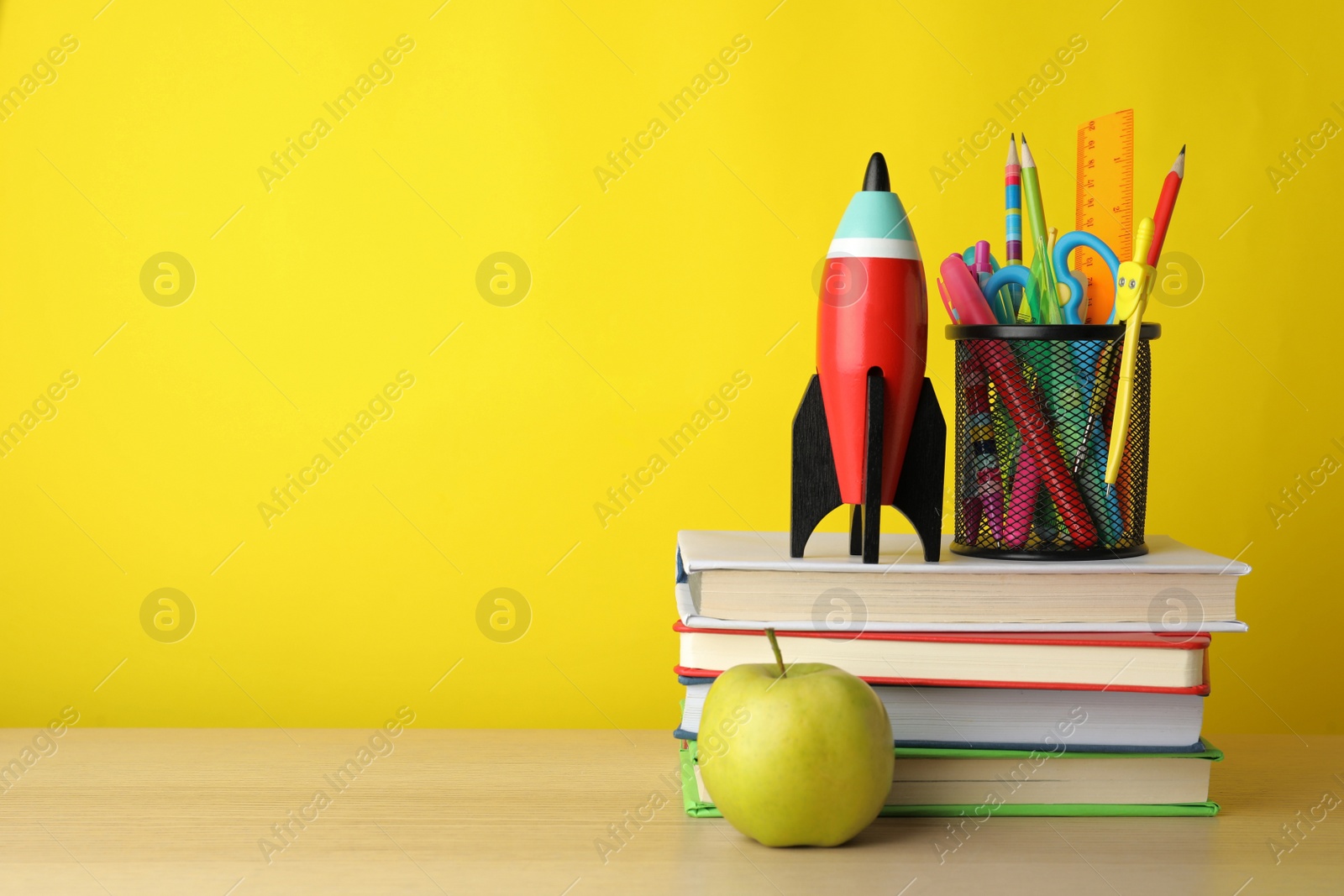 Photo of Bright toy rocket and school supplies on wooden table. Space for text