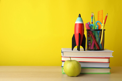 Photo of Bright toy rocket and school supplies on wooden table. Space for text