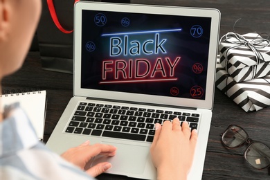 Photo of Woman using laptop with Black Friday announcement at wooden table, closeup