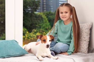 Photo of Cute girl with her dog on window sill indoors. Adorable pet