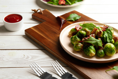 Photo of Delicious Brussels sprouts with bacon on white wooden table