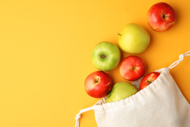 Photo of Cotton eco bag and apples on yellow background, flat lay. Space for text