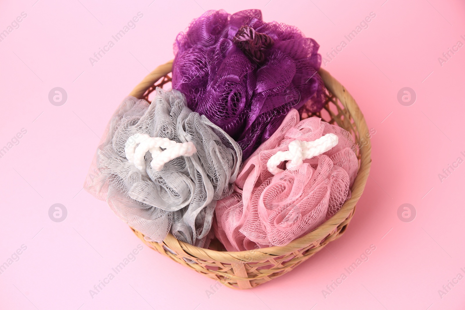 Photo of Wicker basket with colorful shower puffs on pink background, above view