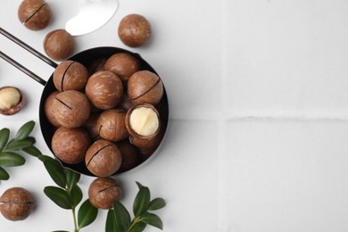 Photo of Tasty Macadamia nuts and green twigs on white tiled table, flat lay. Space for text
