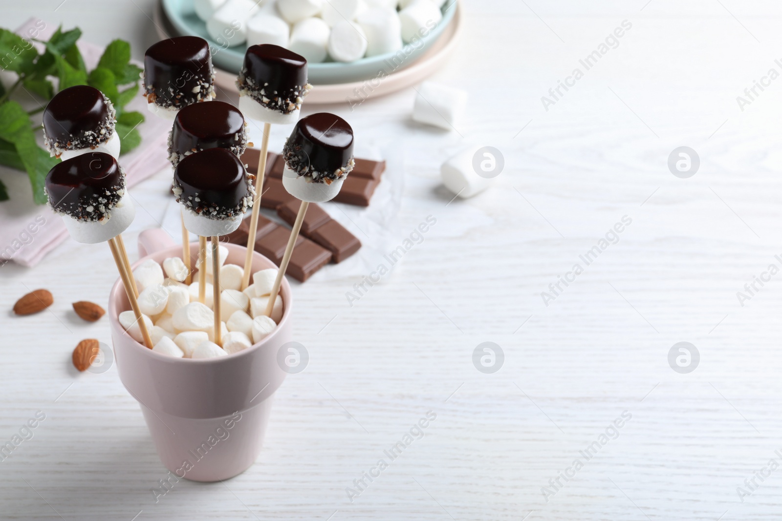 Photo of Delicious marshmallows covered with chocolate on white wooden table. Space for text