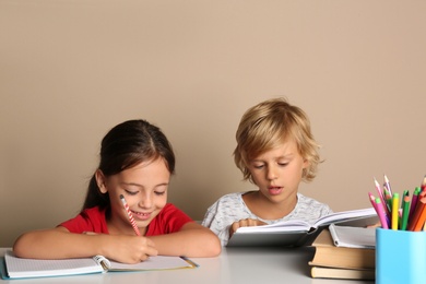 Little boy and girl doing homework at table on beige background