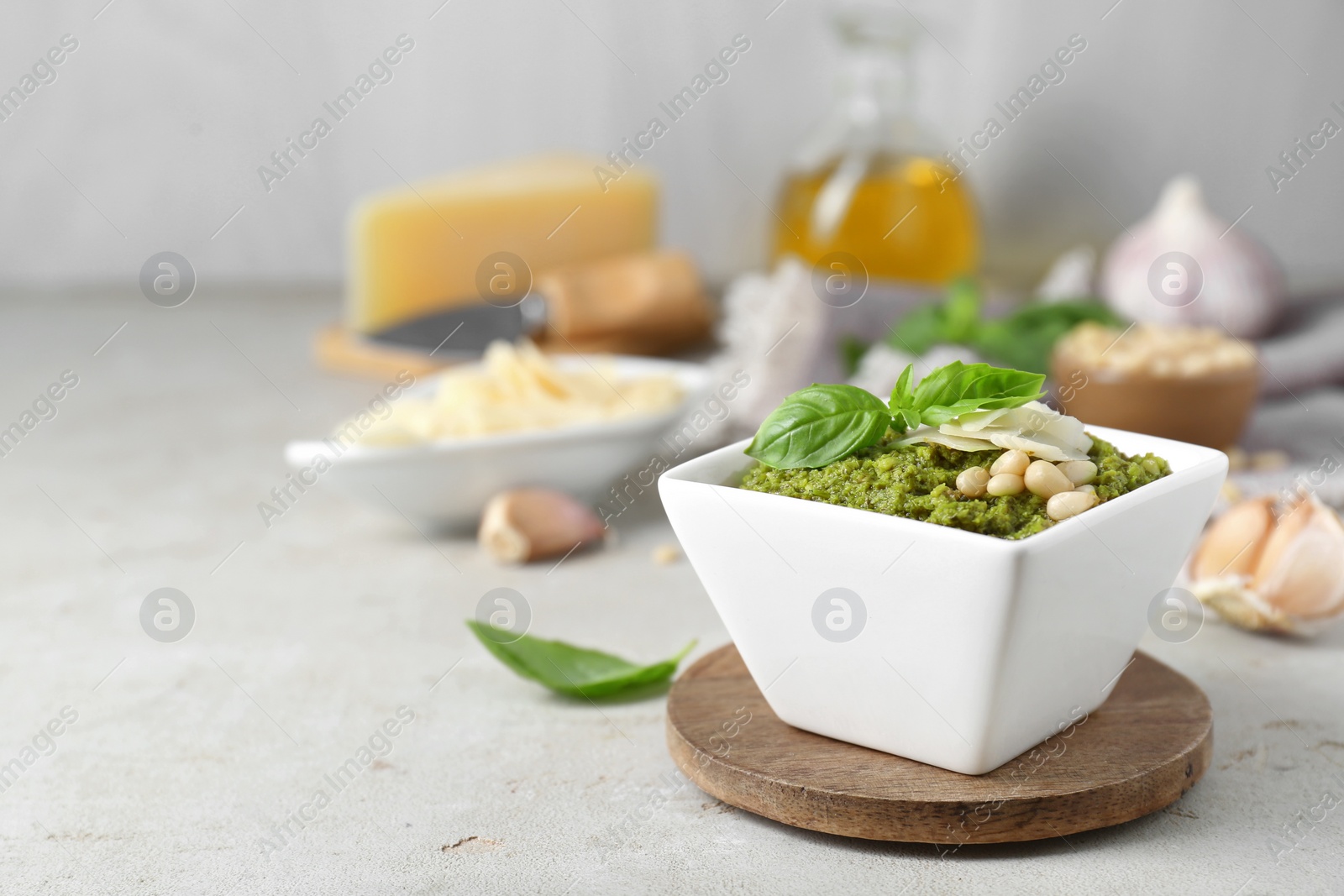 Photo of Bowl with delicious pesto sauce, cheese, pine nuts and basil leaves on light table, closeup. Space for text