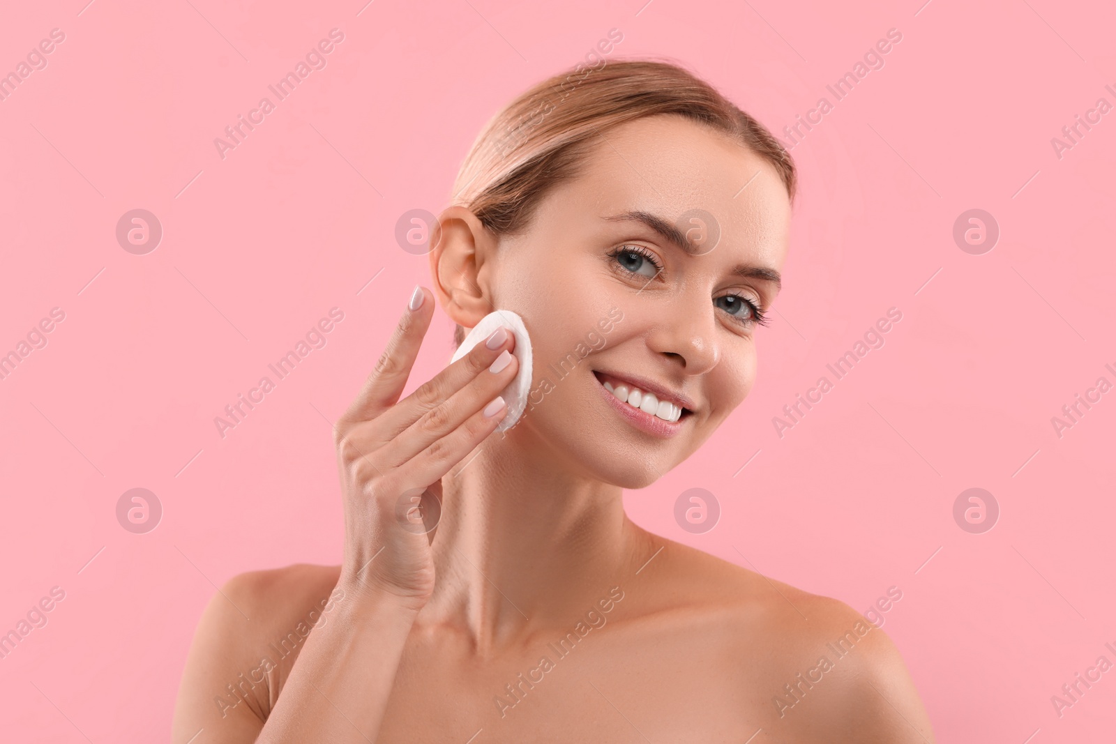 Photo of Smiling woman removing makeup with cotton pad on pink background