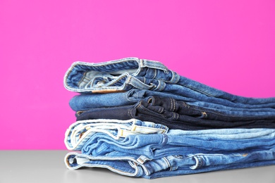 Photo of Stack of jeans on table against color background