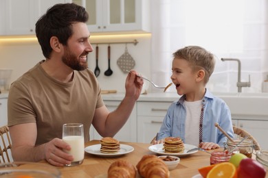 Father and his cute little son having breakfast at table in kitchen