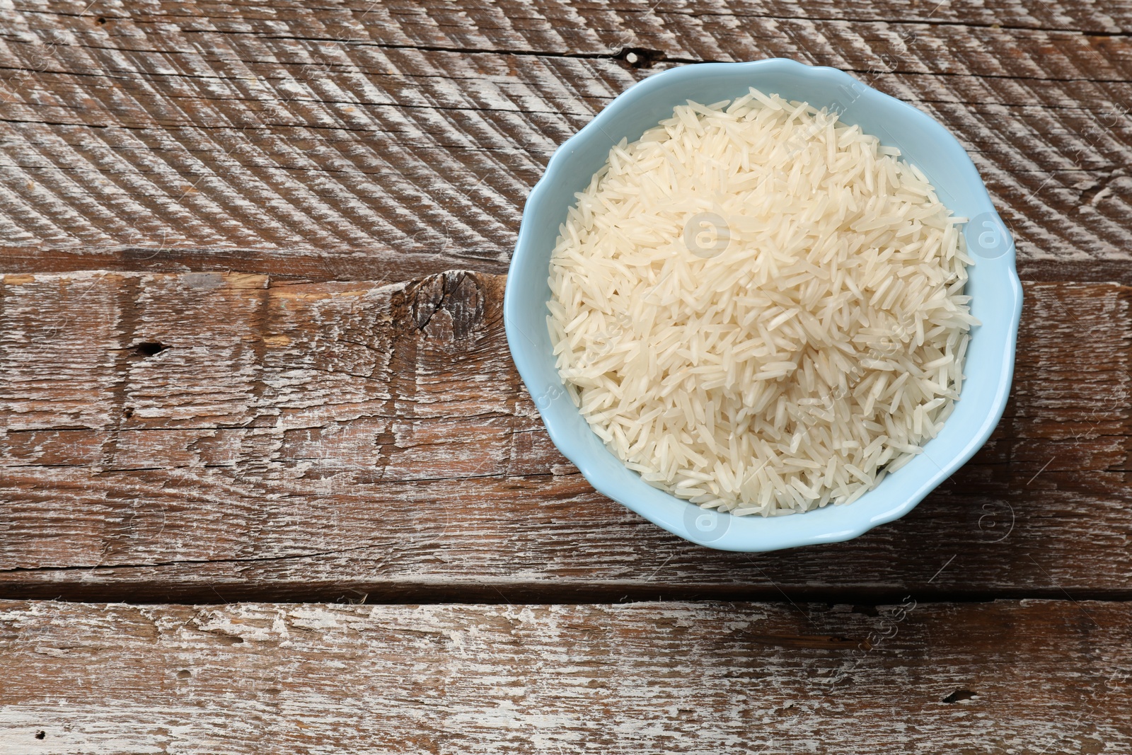 Photo of Raw basmati rice in bowl on wooden table, top view. Space for text