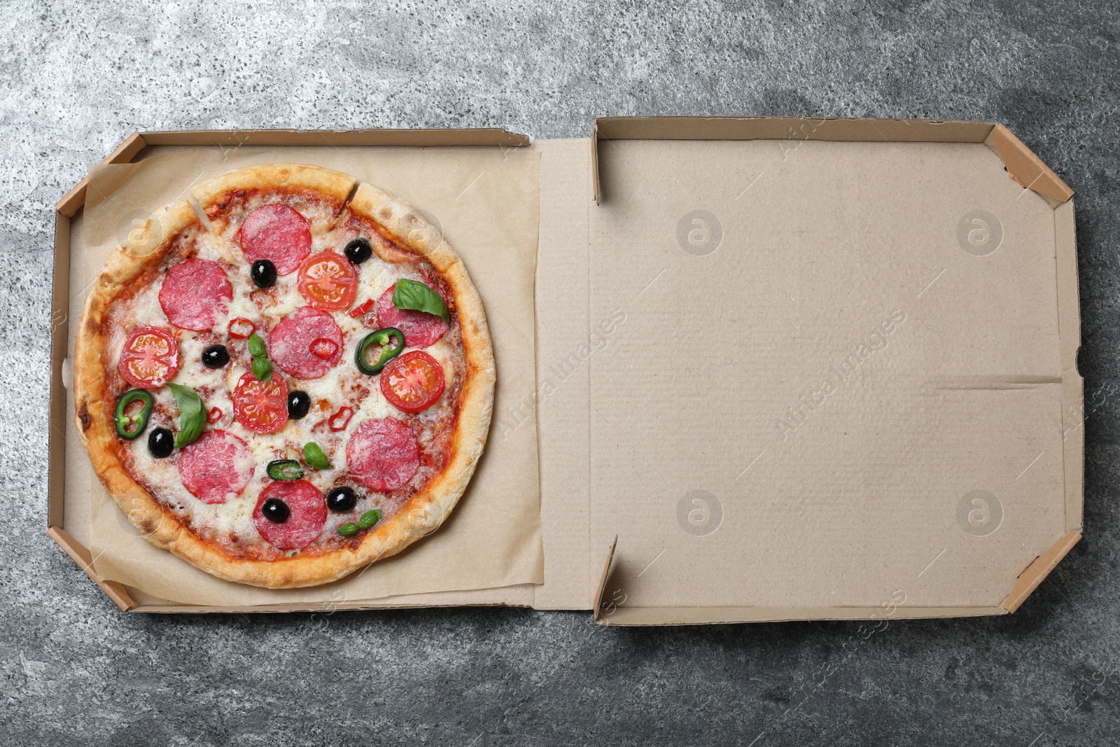 Photo of Delicious pizza Diablo  in cardboard box on dark background, top view