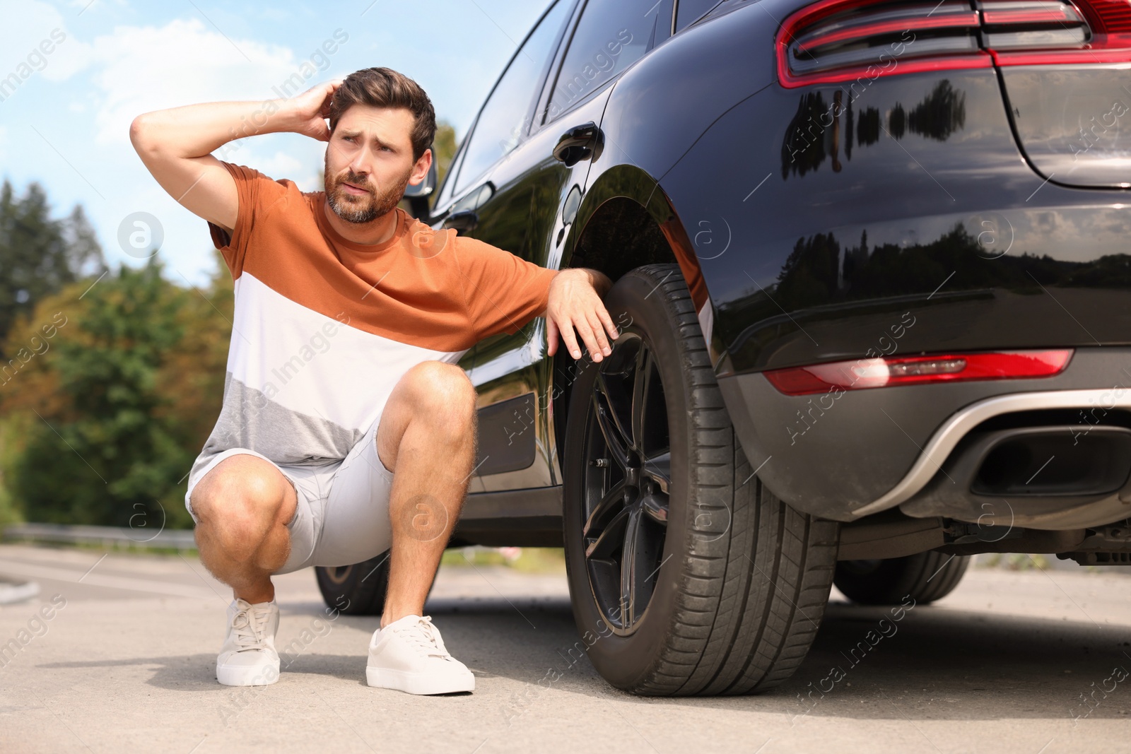 Photo of Tire puncture. Man checking wheel of car on roadside outdoors