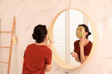 Photo of Young woman applying mask on her face near mirror in bathroom