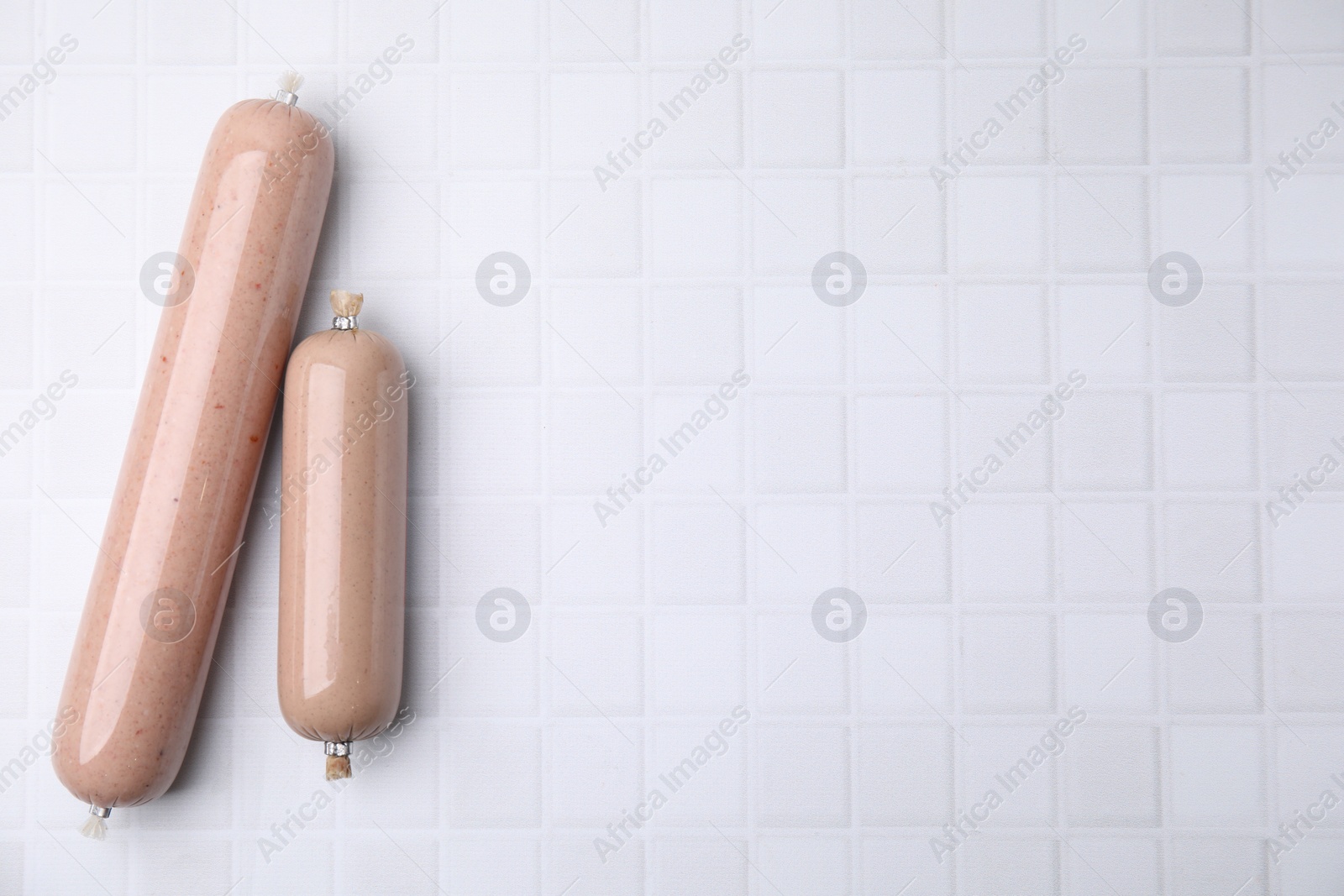 Photo of Delicious liver sausages on white tiled table, flat lay. Space for text