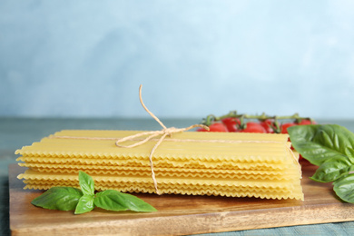 Uncooked lasagna sheets with basil on wooden board